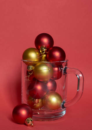 Red and gold Christmas balls lie in a clear glass Cup on a red background