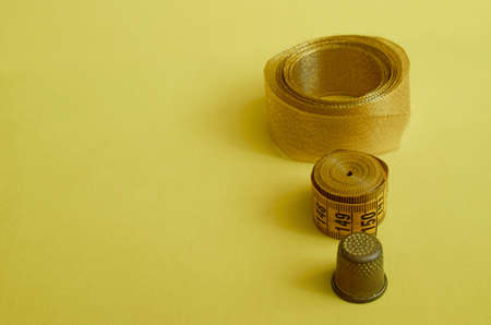 Sewing supplies. Gold ribbon, sartorial meter, thimble close-up on yellow background