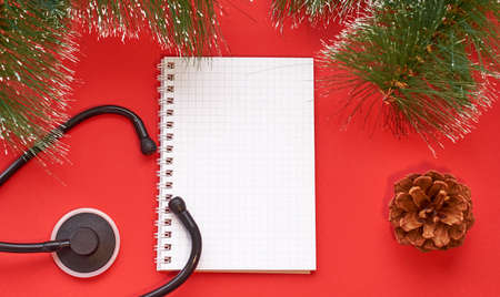 Christmas medical layout. Spruce branch, pine cone, Notepad and medical stethoscope on a red...