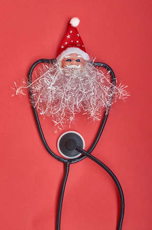 Christmas medical layout. Toy head of Santa Claus with a stethoscope on a red background. Vertical formatの写真素材
