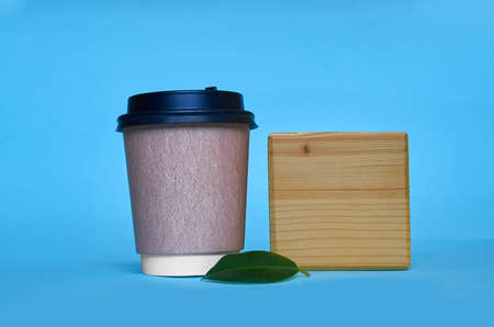 Mock up. A paper cup for coffee, a wooden square and a green ficus leaf