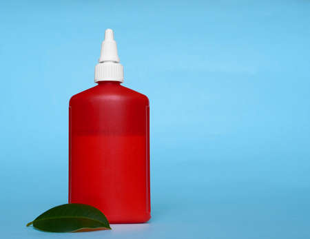 A red tube with a white cap and a green ficus leaf on a blue background. Copy space