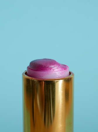 An old used tube of pink lipstick on a blue background. Close-up. Vertical formatの写真素材