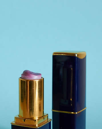 An old used tube of pink lipstick and a closed tube of lipstick on a blue background. Close-up. Vertical formatの写真素材
