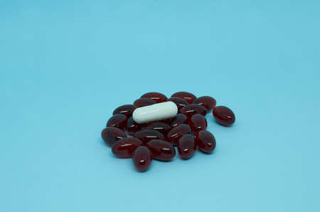 Many dark red capsules and one white capsule are scattered on a blue background