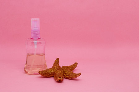 A spray bottle filled with liquid and a starfish on a pink background. Space for textの写真素材