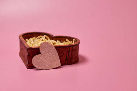 Wooden gift box in the shape of a heart with paper filling and a cardboard heart on a pink...