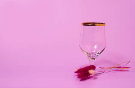 An empty wine glass and a bouquet of dried lagurus flowers on a pink background. Space for textの写真素材
