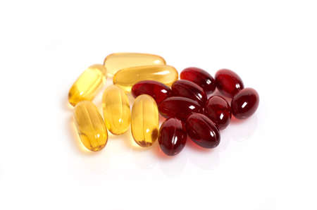 Yellow omega-3 fish oil capsules and red black cumin oil capsules isolated on a white background, selective focus, close upの写真素材