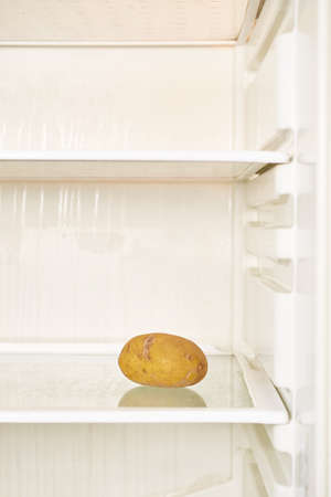 Spoiled potato is on the shelf of an empty refrigerator. Food shortage, vertical formatの写真素材
