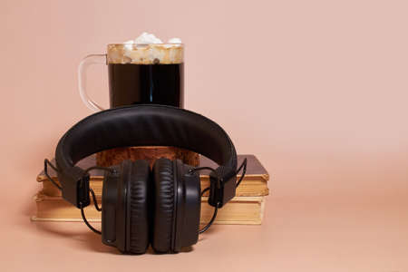 Headphones are lying next to a glass cup of coffee with marshmallows, which stands on a stack of old...