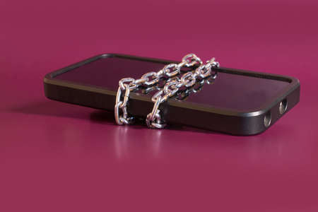 nomophobia. The smartphone is rewound by a chain on a colored backgroundの写真素材