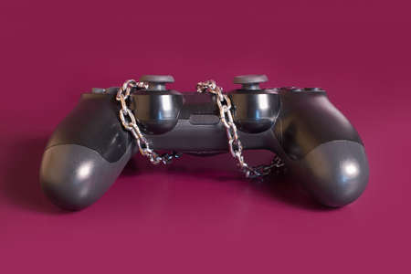 Gambling addiction. The remote from the game console is rewound by a chain on a colored background