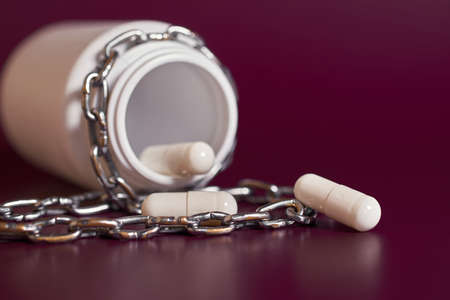drug addiction. A jar with white capsules rewound by a chain on a colored background. selective focusの写真素材