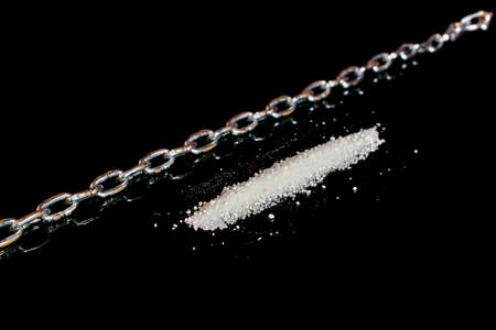 drug addiction. A track of white powder and a chain on a black background with reflection. selective...