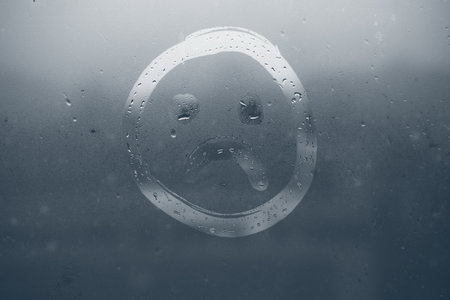 A sad face painted on the fogged glass.の写真素材