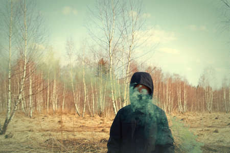 A preteen in a black jacket and a mask holds a checker with colored smokeの写真素材