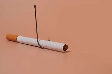 Nicotine addiction. Cigarette with a fish hook on a colored backgroundの写真素材