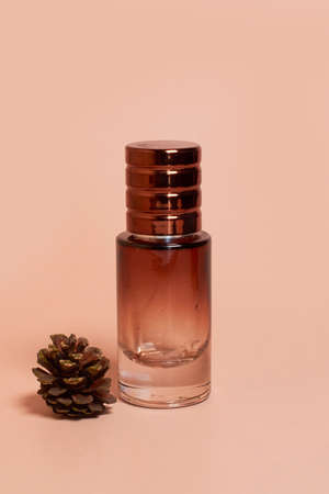 A perfume bottle made of dark glass and a pine cone on a colored background. Space for text,...