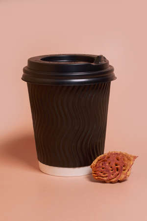 A paper cup with coffee and a peach pit on a colored background. Horizontal format, space for textの写真素材