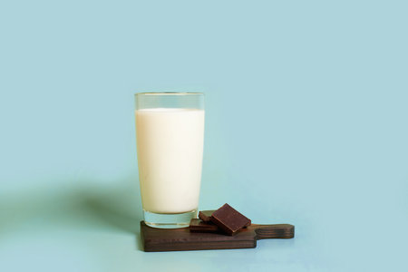 A glass of milk and pieces of dark chocolate on a wooden stand on a colored background. horizontal formatの写真素材