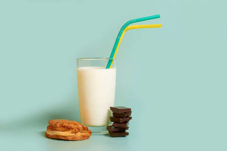 A glass of milk, two plastic tubes, a cake and pieces of dark chocolate on a colored backgroundの写真素材