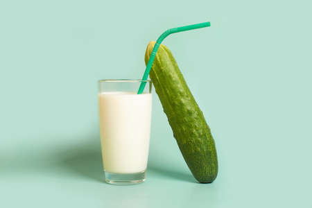 Glass with milk, plastic tube and cucumber on a colored backgroundの写真素材