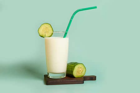 Glass with milk, plastic tube and cucumber slice on a wooden stand on a colored backgroundの写真素材