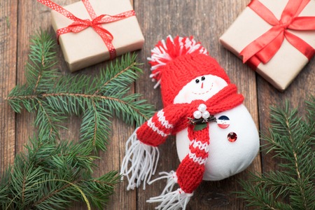 Snowman in a red cap on wooden table with rustic gifts. Christmas decoration. Top view.の写真素材