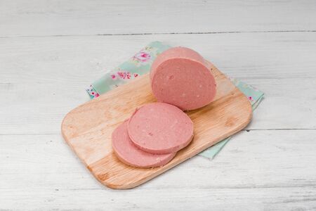 cooked boiled ham sausage or rolled bologna slices on white wooden table.の写真素材