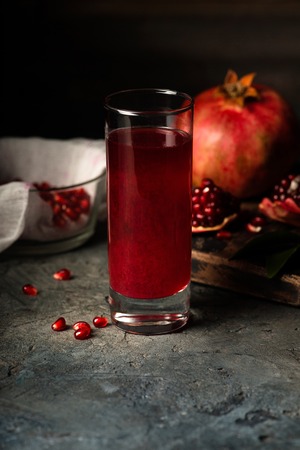 Glass of pomegranate juice.  fruits with grains and leaves on the table. Make . Dark moody.の写真素材