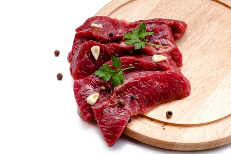 Pieces of meat with garlic and parsley on wooden board isolated. Raw beef. Top view.の写真素材
