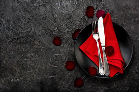 Fork, knife with red napkin, roses and black plate. On dark table background.の写真素材