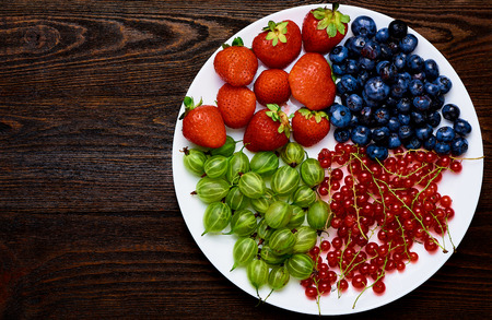 Garden berries on white plate. Strawberries, blueberries, currants, gooseberries on a wooden background. Top view.の写真素材