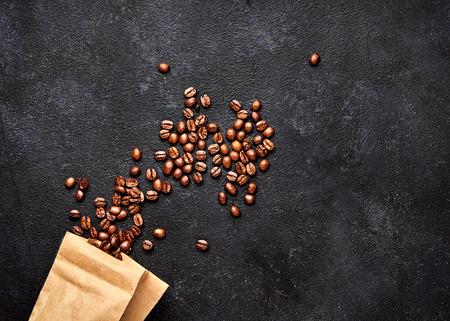 Coffee beans on black concrete background with paper package. Top viewの写真素材