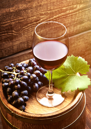 Glass of wine on wooden table with ripe grapes of wine and wooden barrel.の写真素材