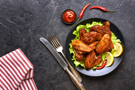 Smoked chicken wings with ketchup and chili hot peppers. Black concrete background. Barbecue. Top view. Space for text.の写真素材