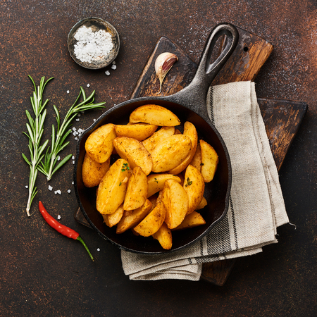 Roast potato with salt and spices in pan on wooden board on brown background with copy space. Top view.の写真素材