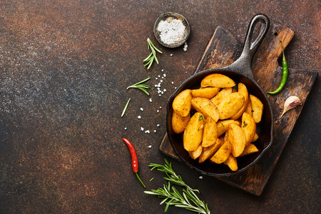 Roast potato with salt and spices in pan on wooden board on brown background with copy space. Top view.の写真素材