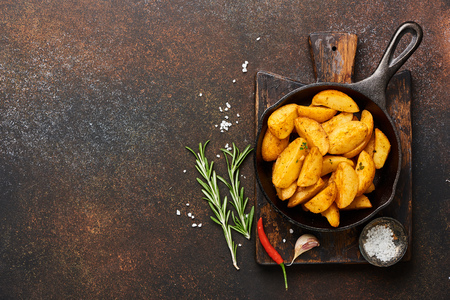 Roast potato with salt and spices in pan on wooden board on brown background with copy space. Top view.の写真素材