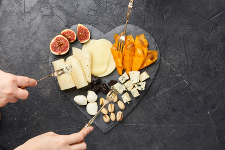 Cheese plate antipasti snack with Blue cheese, olives, figs on black board. Party. hands with forks. Top view.の写真素材