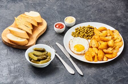 Fried potatoes with fried eggs, green peas on concrete gray backgroundの写真素材