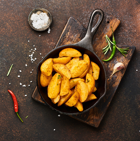 Roast potato with salt and spices in pan on wooden board on brown background with copy space. Top view.の写真素材