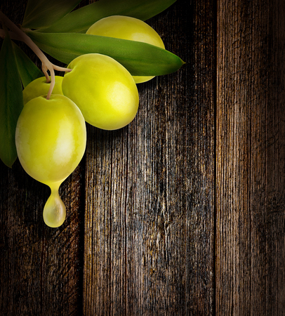 Drop of olive oil falling from one green olive on wooden background with copy space.の写真素材