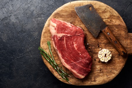Raw fresh marbled meat Black Angus steak and vintage meat cleaver on wooden board. Meat on black background with rosemary and garlic. Copy space. Top view.の写真素材