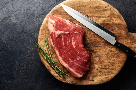 raw fresh marbled meat black angus steak with knife for meat on wooden board. meat on black background with rosemary. copy space. top view.の写真素材