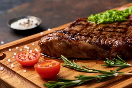 Grilled Black Angus Steak with tomatoes, garlic with chimichurri sauce on meat cutting board.の写真素材