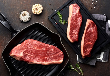 Raw fresh meat Picanha steak, traditional Brazilian cut with thyme, garlic, and black pepper on wooden board. Sliced meat Black Angus steak on grill iron pan. Top view.の写真素材