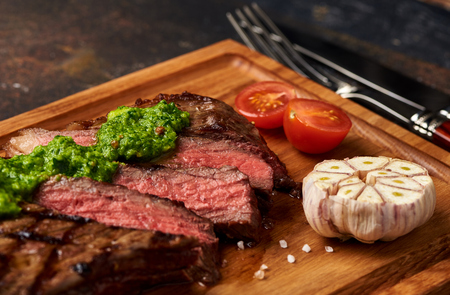 Grilled Black Angus Steak with tomatoes, garlic with chimichurri sauce on meat cutting board.の写真素材