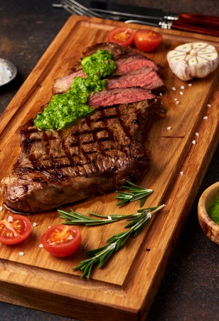 Grilled Black Angus Steak with tomatoes, garlic with chimichurri sauce on meat cutting board.の写真素材